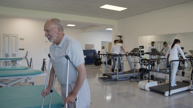 截肢的老年男子行走与男性治疗师的物理治疗，而其他病人的工作背景视频下载