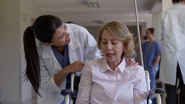 近距离观察坐在轮椅上的高级妇女与友好的医生在医院走廊非常愉快地交谈视频素材