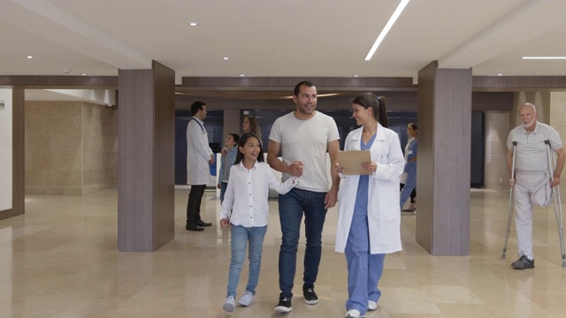 女儿科医生在医院的走廊里与小病人和父亲交谈视频素材