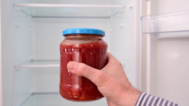 一个男人在冰箱前拿着一罐西红柿。视频下载