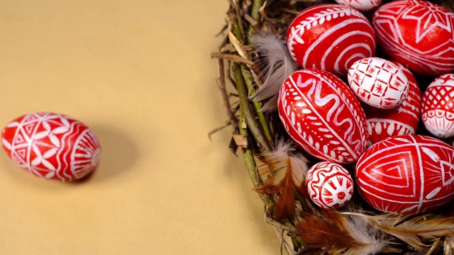 复活节红蛋用民间白色图案编成鸟巢，以纸为背景。人的手为巢添蛋。乌克兰传统鸡蛋pisanka和krashanka。视频素材