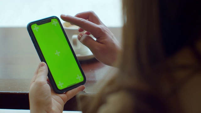 迷人的年轻女子使用她的绿色触摸屏手机在咖啡馆。视频素材