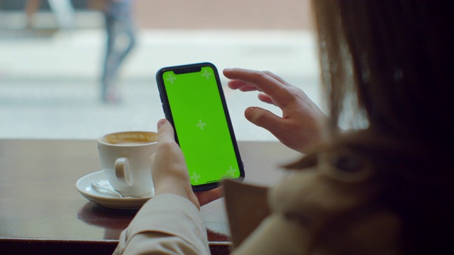 美丽的女人使用绿色触摸屏的手机在咖啡馆。绿色的屏幕。在社交媒体上分享信息。视频素材