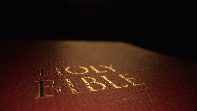 极端微距特写移动滑块显示拍摄的黄金文本标题“圣经”封面纹理图案书的神的话在一个黑暗的背景与独特的照明视频下载