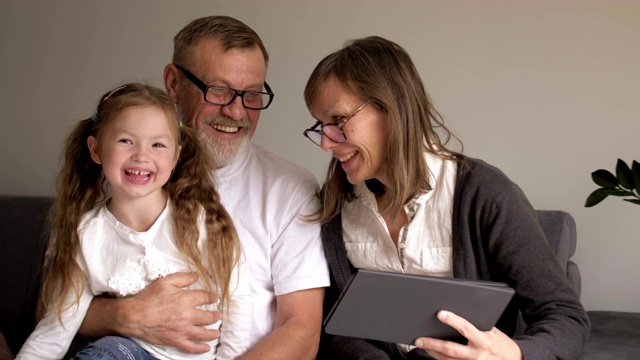 孩子和祖父母在使用平板电脑。一对可爱的中年夫妇和他们的小孙女在家里一起使用数码平板电脑。人才和现代技术视频素材