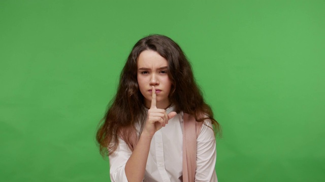安静，不要泄露秘密!迷人的十几岁的黑发女孩在白衬衫把手指放在嘴唇上，显示沉默的手势视频下载