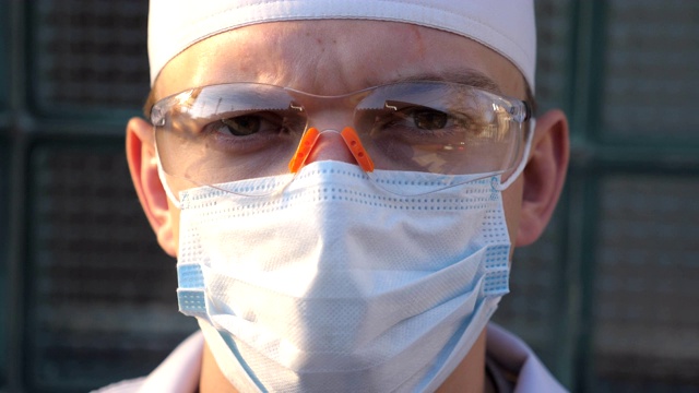 年轻男性白人医生的肖像与医疗面罩看着相机。医护人员戴着防护口罩以防病毒。应对冠状病毒大流行的健康和安全生命理念。新型冠状病毒肺炎视频下载