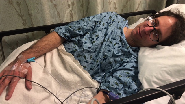 一名男子躺在医院病床上，正在用手输液视频素材