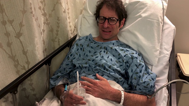 一名男子躺在医院的病床上，一边抱着水一边痛得抓着肚子视频素材