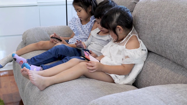 三个孩子在家里的沙发上使用数字设备。视频素材