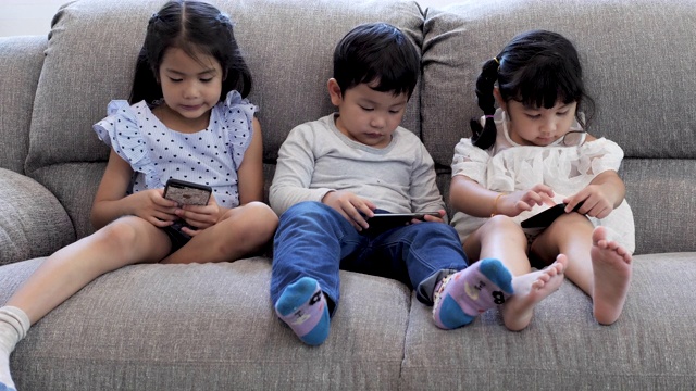 三个孩子在家里的沙发上使用数字设备。视频素材