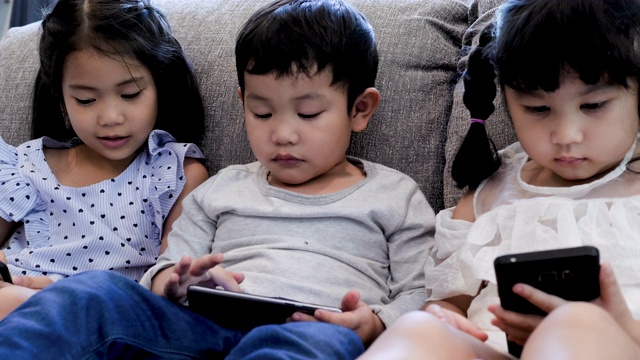 三个孩子在家里的沙发上使用数字设备视频素材