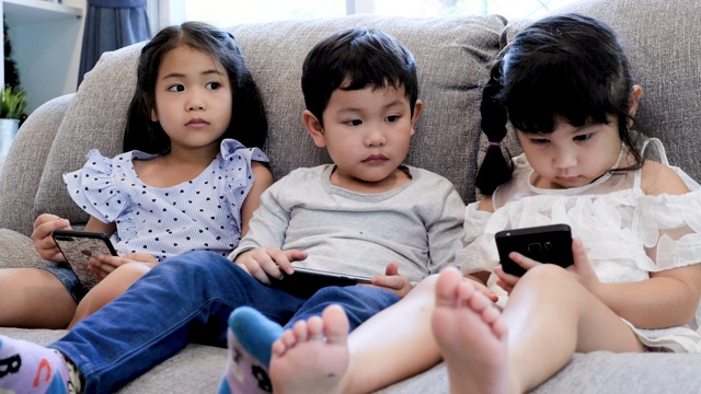三个孩子在家里的沙发上使用数字设备视频素材