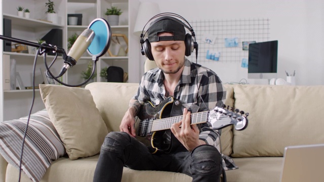 在沙发上弹吉他和录制歌曲的男人视频下载