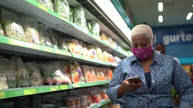 戴着口罩在超市行走和使用手机的妇女视频下载