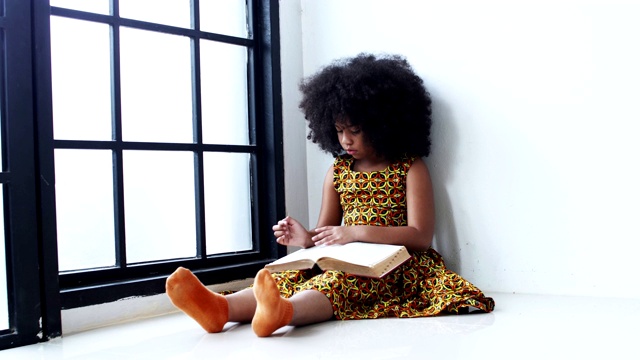 一个非洲女孩坐在角落里看书。视频下载