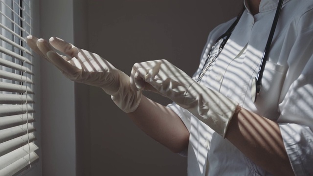 护士在窗边戴上医用手套。股票视频视频素材