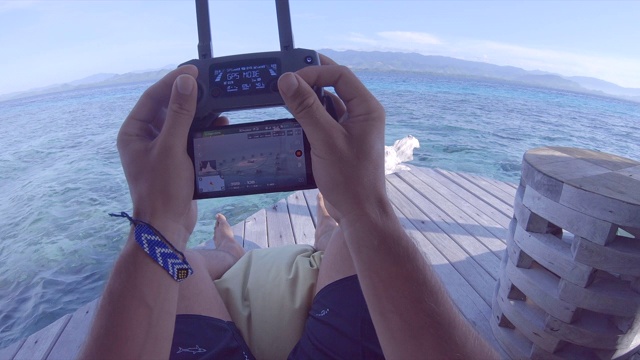 一名男子在一个岛屿度假酒店使用遥控和智能手机驾驶无人机进行航拍。视频素材