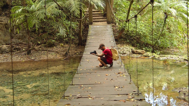 一名男子在吊桥上拍照。墨西哥帕伦克玛雅遗址自然公园视频下载