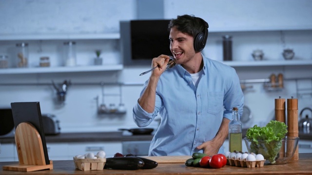 兴奋的男人戴着无线耳机和新鲜的食材在桌边跳舞视频下载