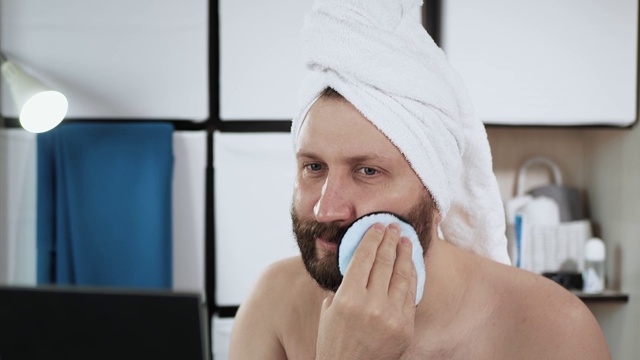 男人用海绵洗脸。可笑的是，年轻英俊的白人男子在浴室里看着镜子，然后用海绵擦脸。特写镜头视频下载