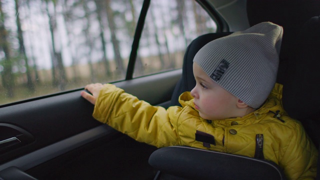一个2岁的白人男孩向车窗外看。一个两岁的白人男孩坐在他的座位上，看着窗外的一辆移动的车辆。视频素材
