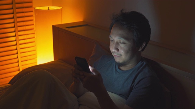 亚洲男人晚上在床上玩智能手机视频素材