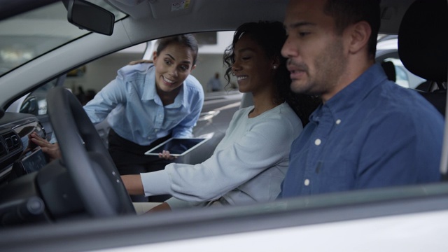 售货员在一个经销商展示一辆汽车给一对幸福的多样化的夫妇试图做销售视频下载