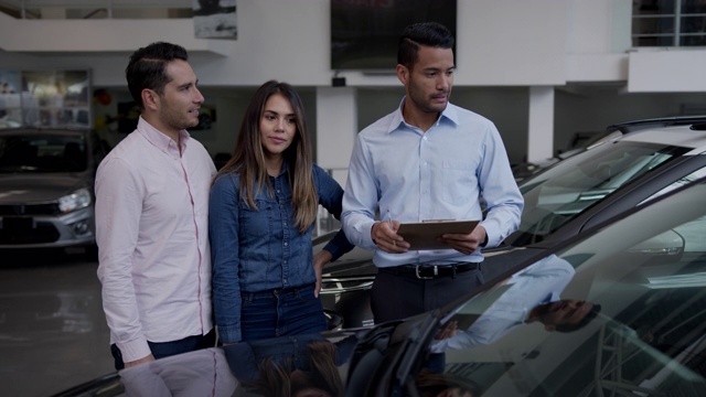 快乐的夫妇听着友好的推销员解释关于汽车的一些事情，他们都看起来很兴奋视频素材