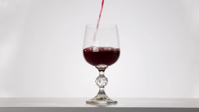 特写镜头。红酒正倒入玻璃杯中。白色背景。4 k视频素材