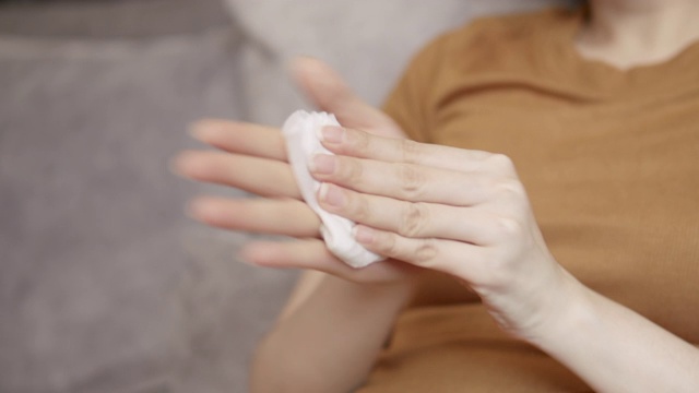 亚洲妇女清洁她的脏手与婴儿擦纸。成年妇女坐在沙发上用白色湿纸巾擦手。保健、卫生、美容理念。视频素材