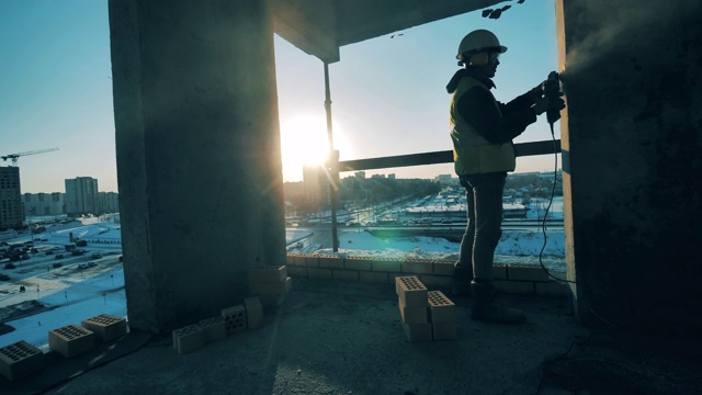 一名男工人正在打磨一座在建的多层建筑的墙壁。建筑工地的建筑工人。视频素材