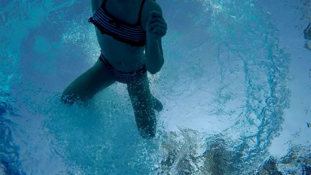 一个穿着条纹泳衣的女孩用手捂着鼻子跳进水里。在水下拍摄视频下载