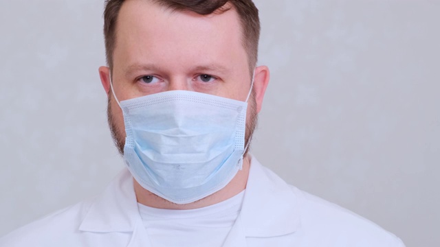一名戴着防护面具、身穿白衬衫的男子看着镜头，特写镜头。卫生的概念。防止细菌和细菌的传播，避免感染冠状病毒视频下载