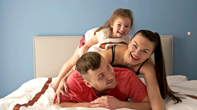 有趣的家庭。爸爸，妈妈和小女儿在床上玩视频下载