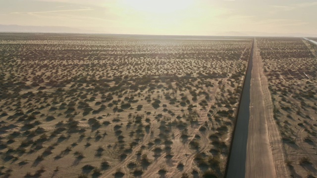 一个阳光明媚的下午，在加州/墨西哥沙漠中，远处的群山为背景，一条与墨西哥和美国之间的钢条边境墙平行的土路视频下载