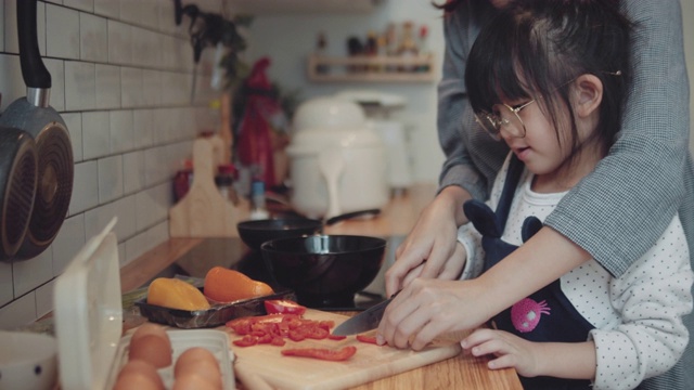 千禧妈妈在厨房准备早餐，而她的女儿在家里帮忙做煎蛋卷。视频素材