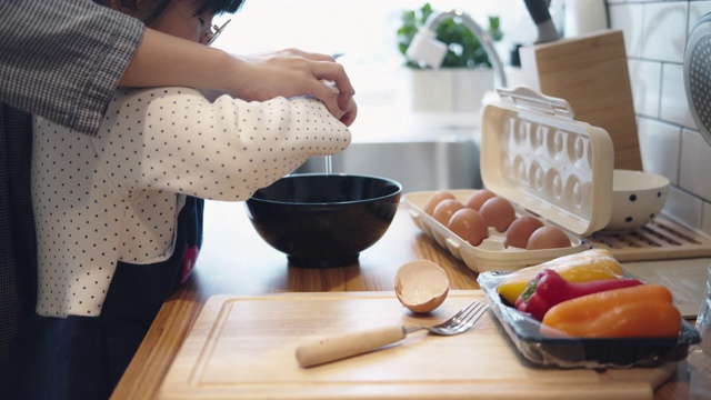 千禧妈妈在厨房准备早餐，而她的女儿在家里帮忙做煎蛋卷。视频素材