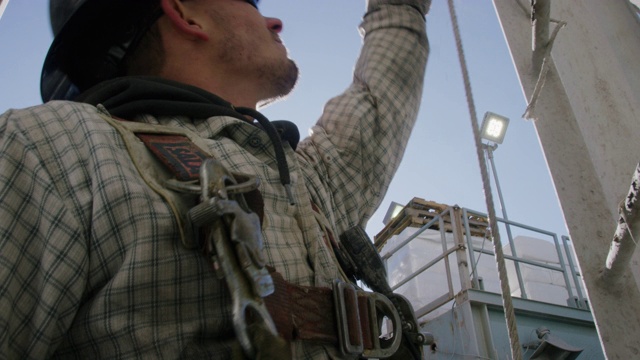 一个阳光明媚的早晨，一名二十多岁的男油田工人在检查泥浆罐侧面的梯子上的安全电缆视频下载