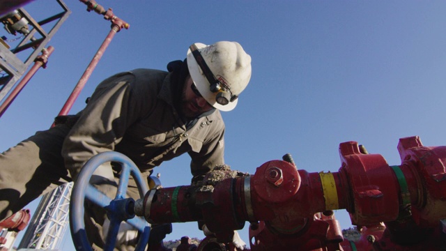 慢镜头拍摄的一个油田工人在他三十多岁在一个寒冷的，阳光明媚的冬天早晨在石油和天然气钻井平台上泵下管线视频素材