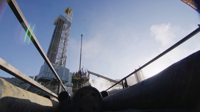 一个寒冷的，阳光明媚的，冬天的早晨，油田工人在石油和天然气钻井平台的一个高高的，金属平台上架设钻杆的广角镜头视频素材