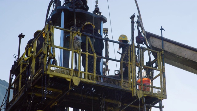 一个寒冷、阳光明媚的冬天早晨，油田工人在一个石油和天然气钻井平台上维修一口井的慢镜头视频素材