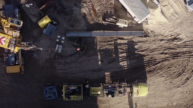 在一个阳光明媚的日子里，一架无人机在山谷里的一个石油和天然气钻井平台上直接拍摄了起重机拆卸钻机的画面视频素材