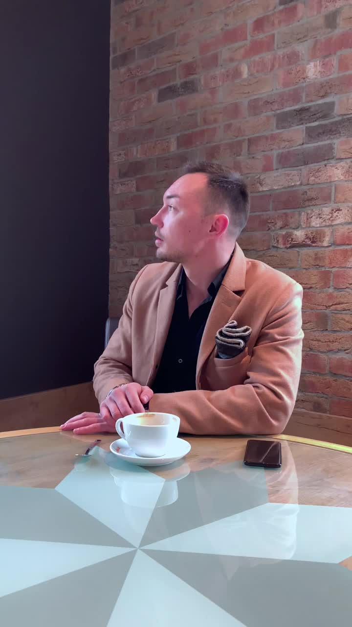 垂直视频，一个帅哥独自在咖啡馆喝咖啡，在智能手机上写作视频素材