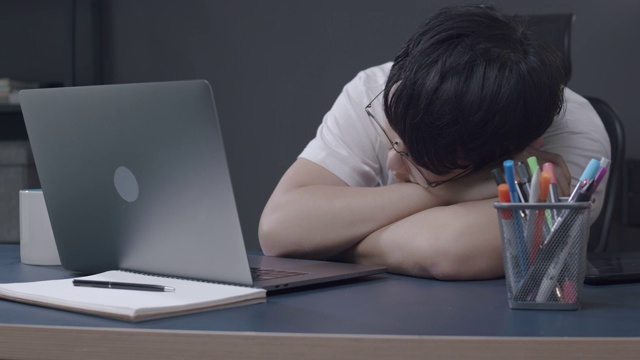亚洲男人在工作过度的家庭办公室睡觉。他工作累了，在家工作时打了个盹。视频素材