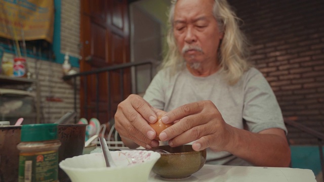 一位留着白色长发的亚洲老人正在餐桌上为家人准备煮熟的鸡蛋。视频素材