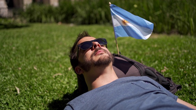 帅哥在阿根廷国旗旁的公园里晒日光浴视频下载