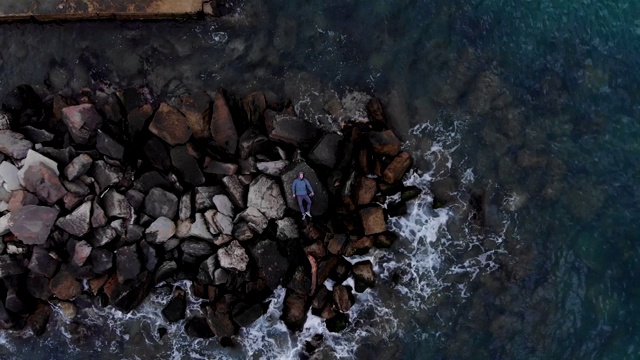 从空中俯瞰，一个孤独的男人躺在防波堤的石头上视频素材