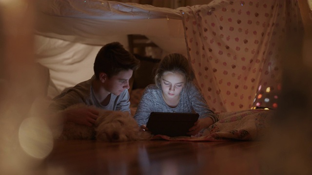 哥哥和妹妹在枕头堡垒里玩平板电脑。视频下载