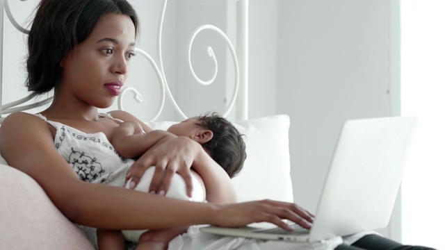 母亲抱着孩子，通过床上的笔记本电脑从家里开始工作。视频下载
